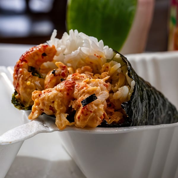 A close-up of a Hawaiian hand roll with rice and spicy seafood, served in a white container.