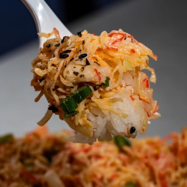A spoonful of Hawaiian poke with rice, crab, green onions, and black sesame seeds.