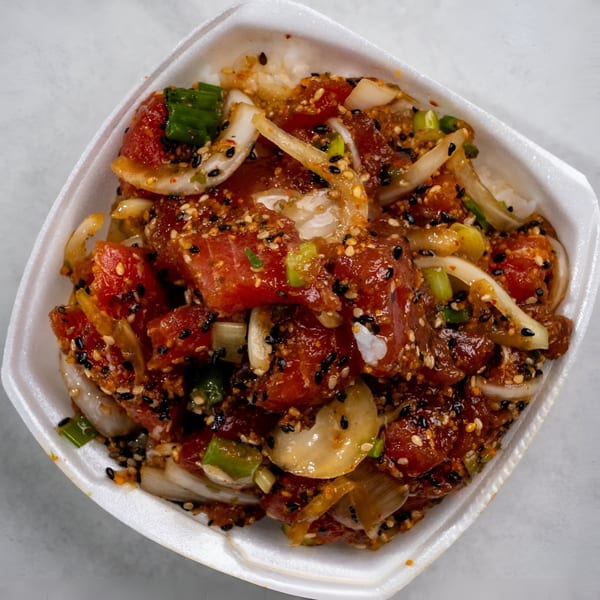 Noble House Hawaiian Restaurant's poke bowl with tuna, onions, and sesame seeds in a white container.