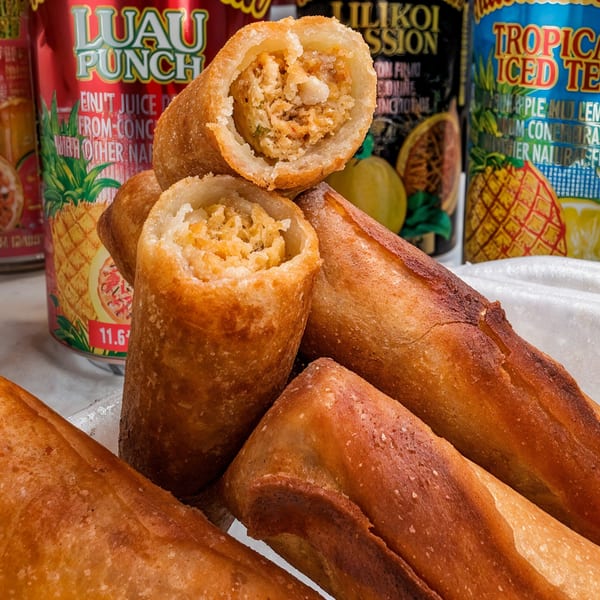 Golden-brown Hawaiian spring rolls, one cut open to show the filling, with tropical drink cans in the background.